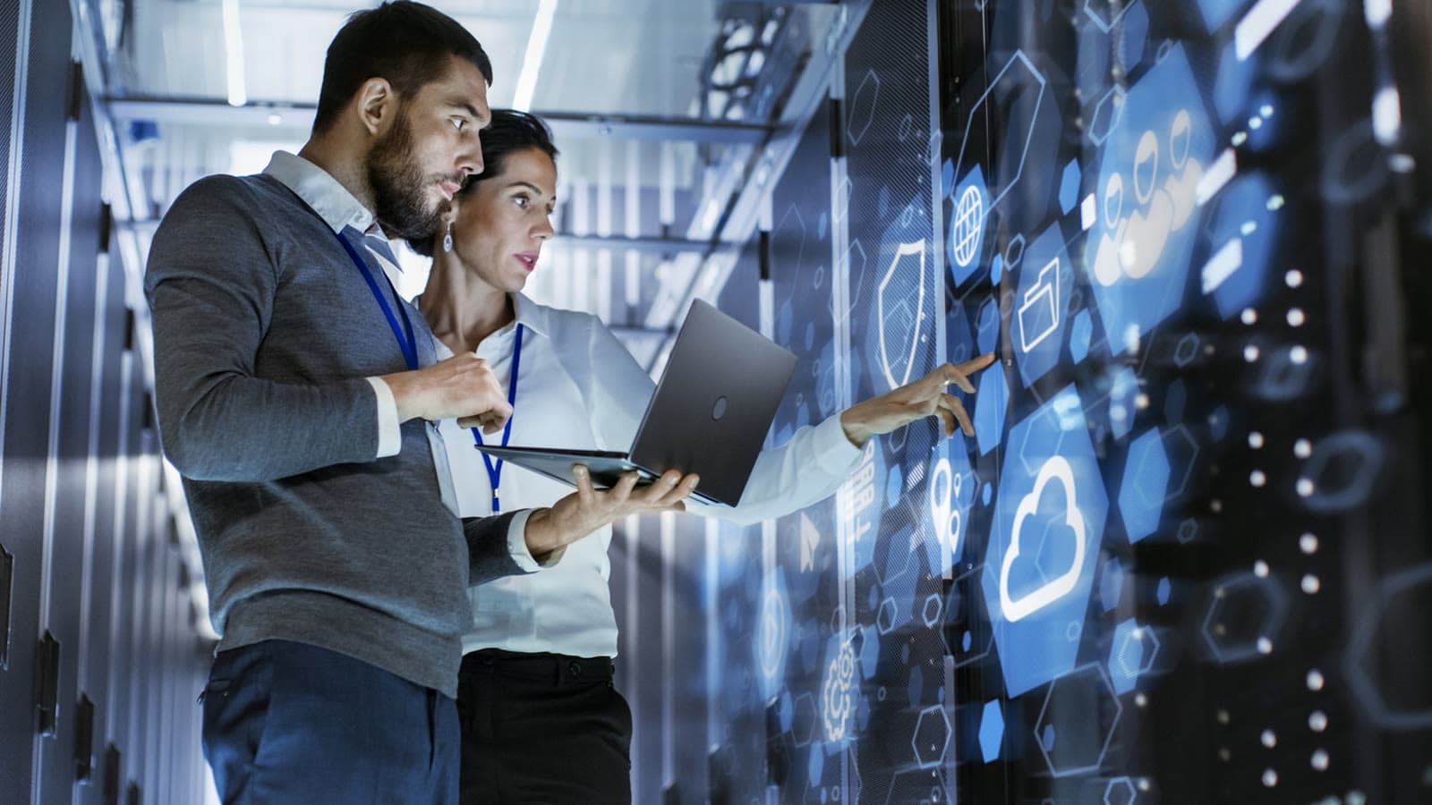 Two IT specialists with a laptop in a data centre, pointing at cloud icons
